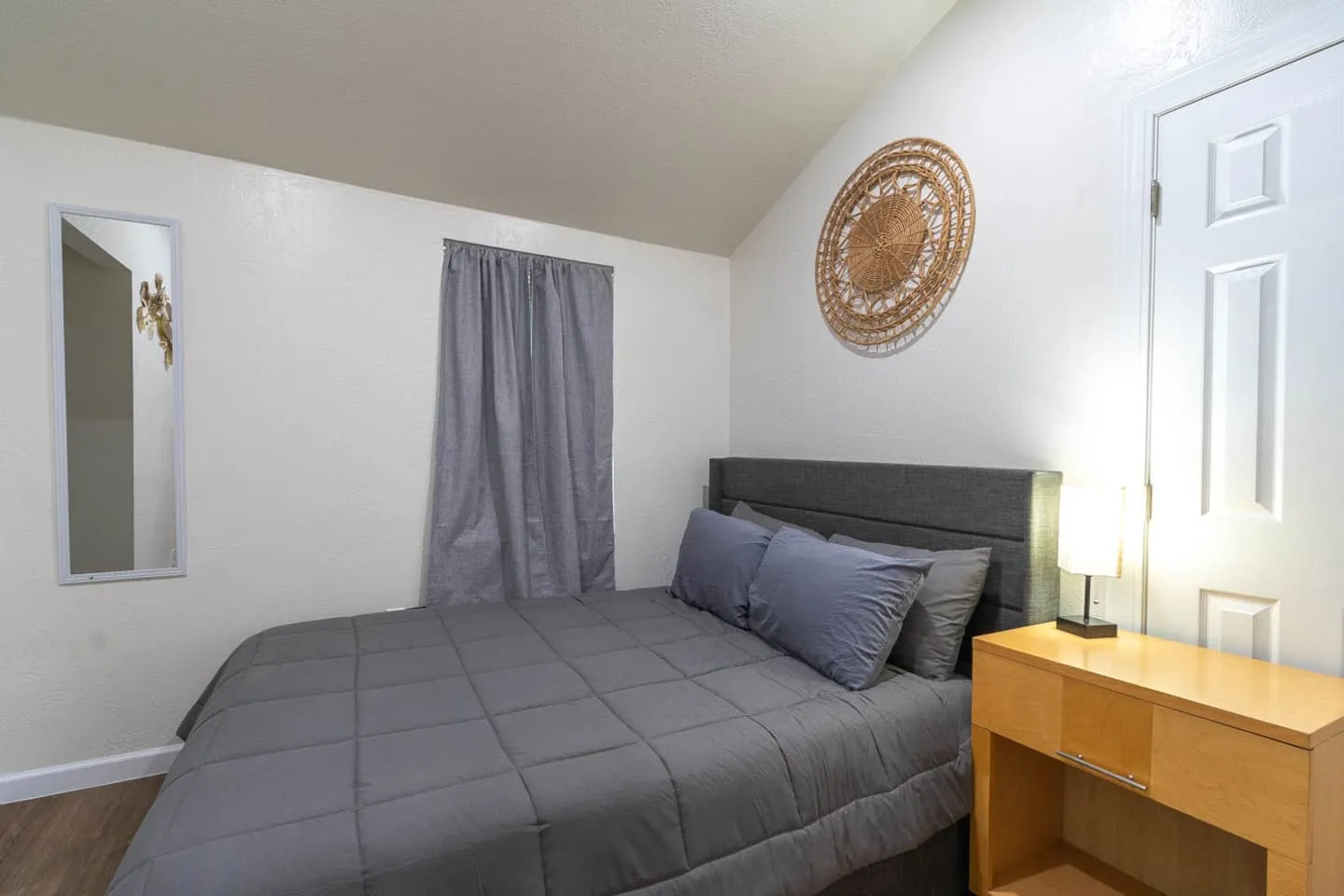 Unit 4 bedroom with gray bedding, a nightstand and woven wall decor