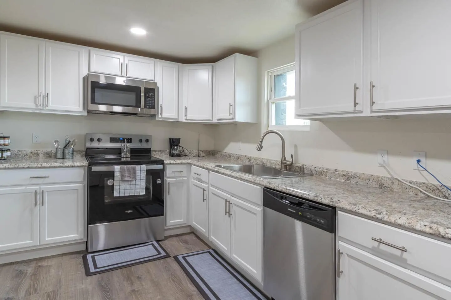 Unit 5 kitchen with white cabinets, granite counters, a stove and microwave
