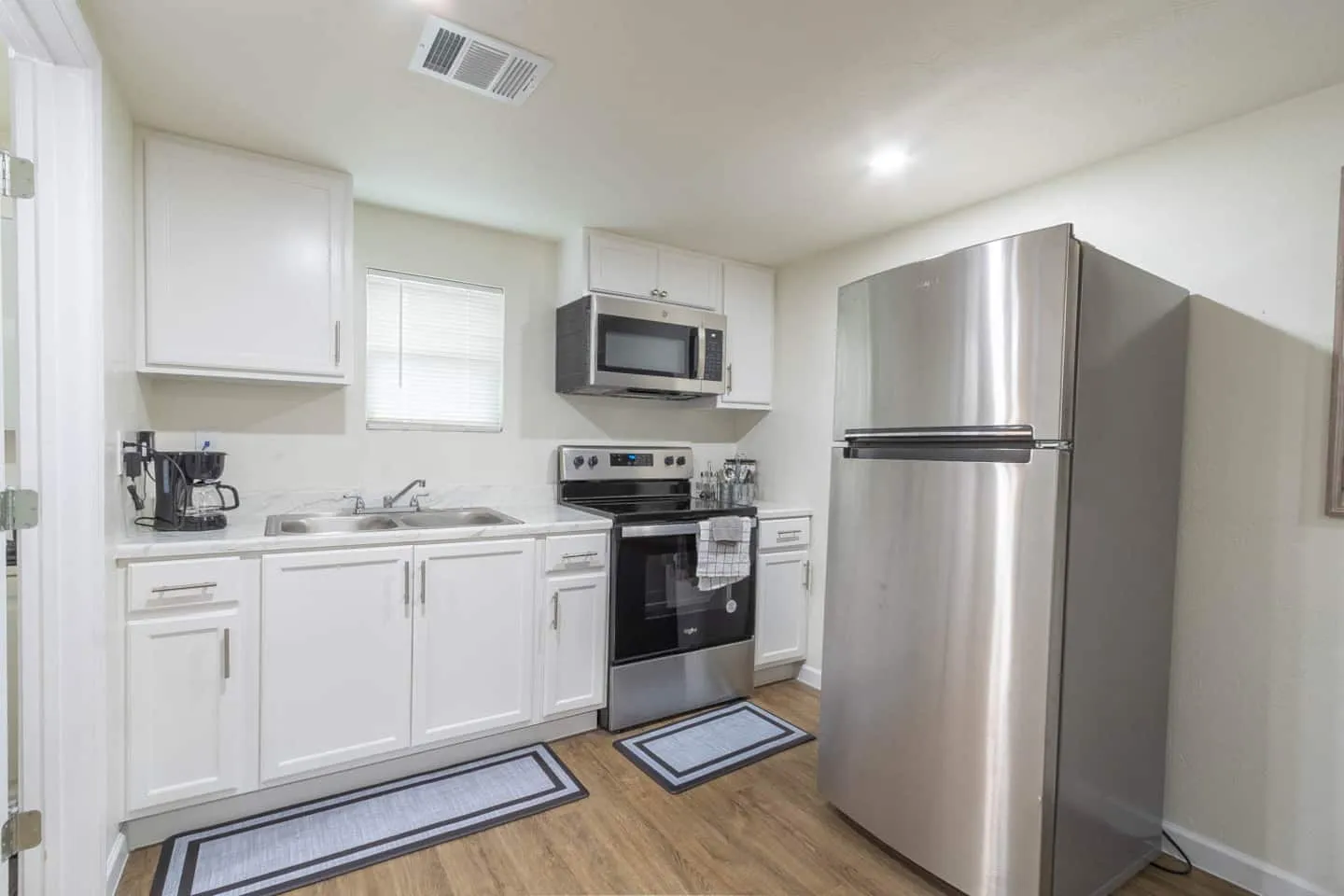 Unit 1 kitchen with white cabinets, a stove, microwave and stainless steel refrigerator
