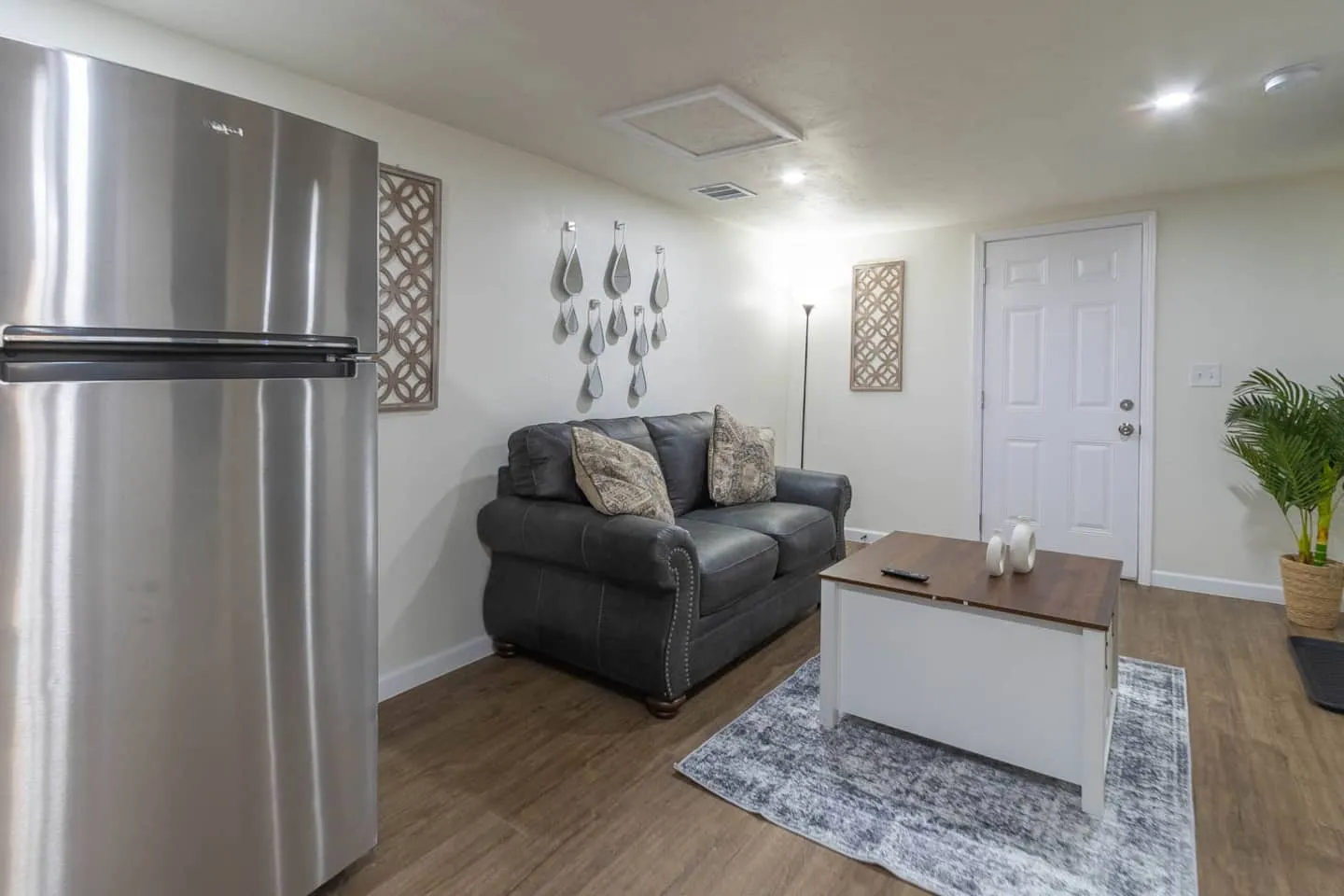 Unit 1 living room with a gray sofa, coffee table, rug and stainless steel refrigerator