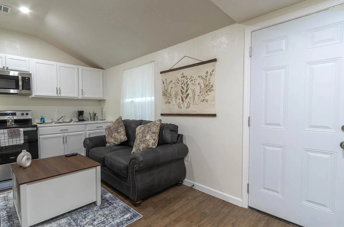 Unit 4 living room with a gray loveseat, coffee table and the kitchenette behind